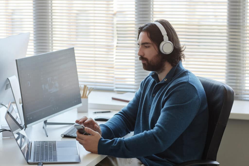 Young man in headphones using mobile phone during work with data