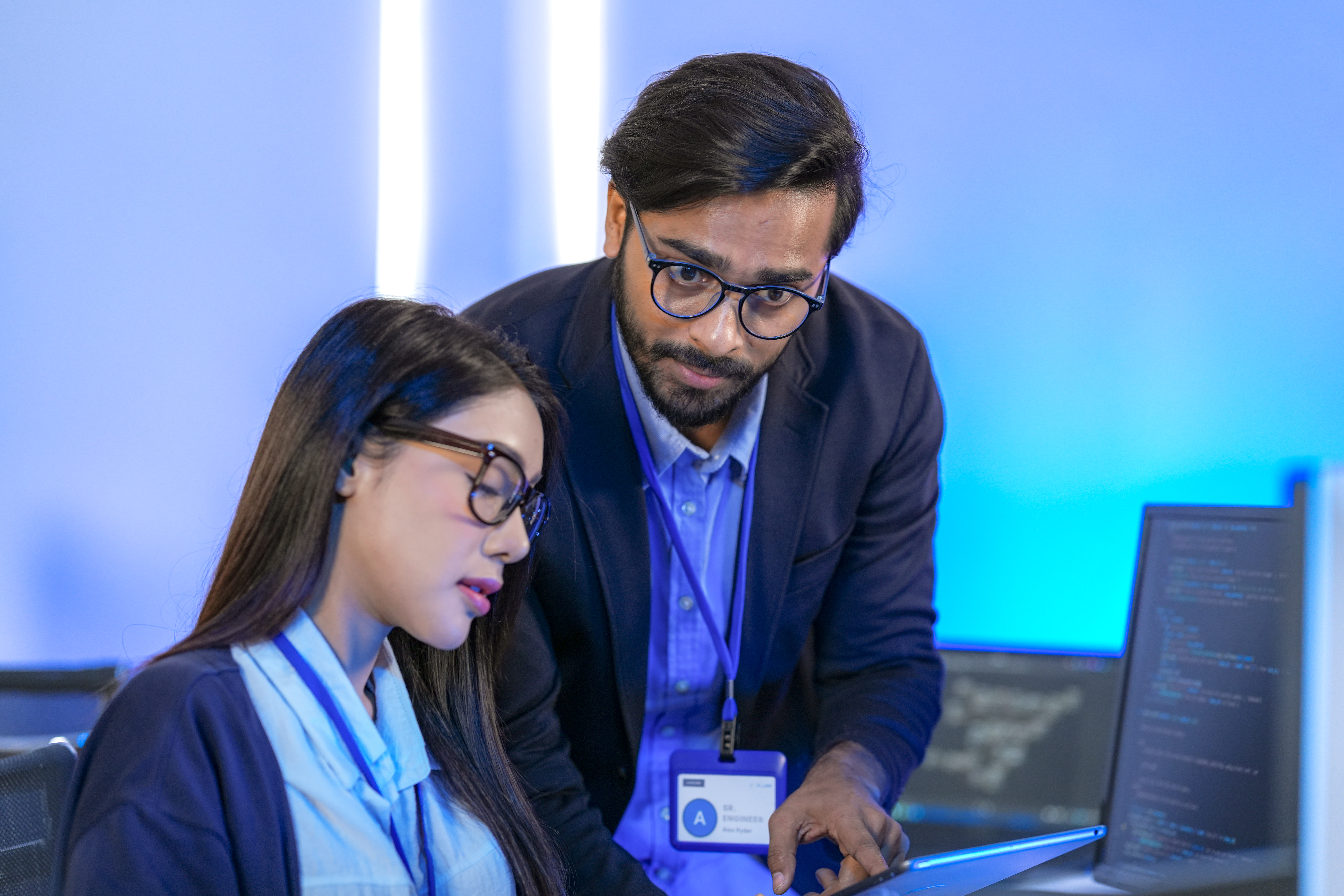 Diverse tech team collaborate, using a desktop for coding and a tablet for input.